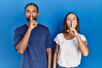 Poster - Young hispanic couple standing together asking to be quiet with finger on lips. silence and secret concept.