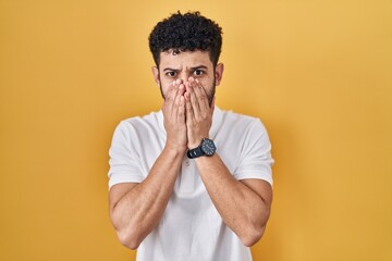 Wall Mural - Arab man standing over yellow background shocked covering mouth with hands for mistake. secret concept.