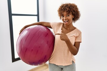 Canvas Print - Young african american woman holding pilates ball smiling happy pointing with hand and finger