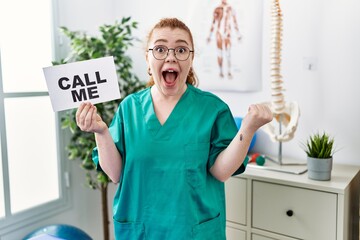 Poster - Young redhead doctor woman working at pain recovery clinic holding call me banner screaming proud, celebrating victory and success very excited with raised arms