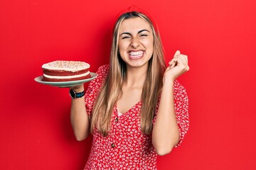 Poster - Beautiful hispanic woman holding strawberry cake screaming proud, celebrating victory and success very excited with raised arm