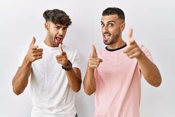 Poster - Young gay couple standing over isolated background pointing fingers to camera with happy and funny face. good energy and vibes.