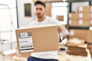 Wall Mural - Young hispanic man working at small business ecommerce holding box clueless and confused expression. doubt concept.