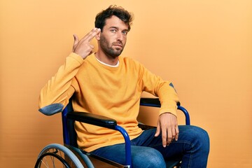 Poster - Handsome man with beard sitting on wheelchair shooting and killing oneself pointing hand and fingers to head like gun, suicide gesture.