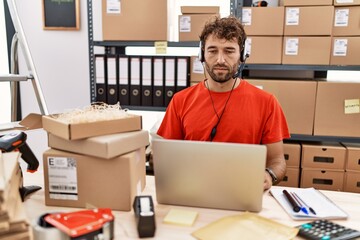 Poster - Young hispanic call center agent man working at warehouse relaxed with serious expression on face. simple and natural looking at the camera.