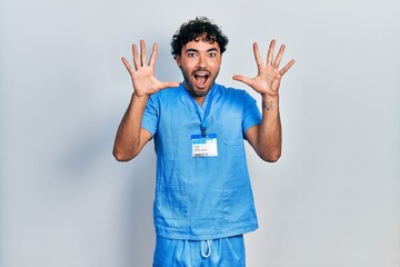 Poster - Young hispanic man wearing blue male nurse uniform celebrating crazy and amazed for success with arms raised and open eyes screaming excited. winner concept