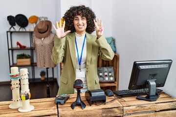 Poster - Young middle eastern woman working as manager at retail boutique showing and pointing up with fingers number eight while smiling confident and happy.