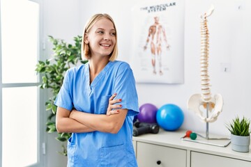 Canvas Print - Young blonde woman wearing physiotherapist uniform standing with arms crossed gesture at rehab clinic