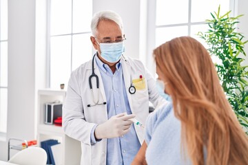 Canvas Print - Middle age man and woman doctor wearing medical mask vaccinating patient at clinic