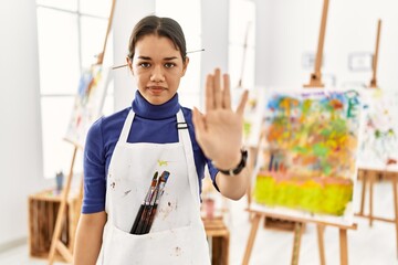 Canvas Print - Young brunette woman at art studio doing stop sing with palm of the hand. warning expression with negative and serious gesture on the face.