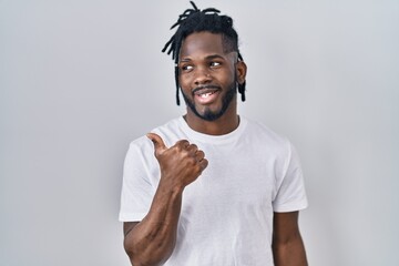 Wall Mural - African man with dreadlocks wearing casual t shirt over white background smiling with happy face looking and pointing to the side with thumb up.