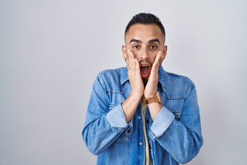 Poster - Young hispanic man standing over isolated background afraid and shocked, surprise and amazed expression with hands on face