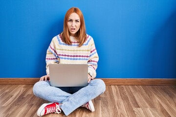 Sticker - Young woman using laptop at home sitting on the floor in shock face, looking skeptical and sarcastic, surprised with open mouth