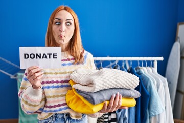 Canvas Print - Young woman holding donations for charity making fish face with mouth and squinting eyes, crazy and comical.