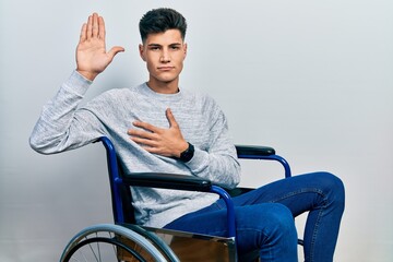 Wall Mural - Young hispanic man sitting on wheelchair swearing with hand on chest and open palm, making a loyalty promise oath