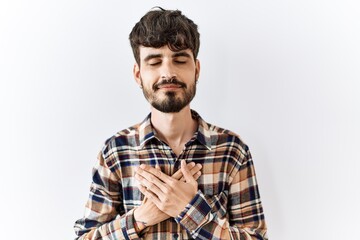 Poster - Hispanic man with beard standing over isolated background smiling with hands on chest with closed eyes and grateful gesture on face. health concept.