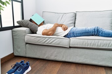 Sticker - Young hispanic man lying on sofa sleeping with book on face at home