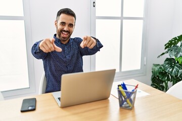 Sticker - Young hispanic man with beard working at the office with laptop pointing to you and the camera with fingers, smiling positive and cheerful