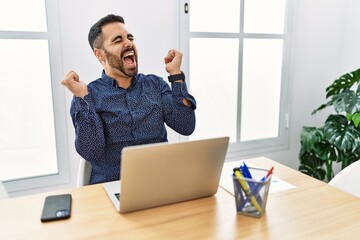 Poster - Young hispanic man with beard working at the office with laptop celebrating surprised and amazed for success with arms raised and eyes closed. winner concept.