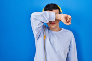 Canvas Print - Non binary person listening to music using headphones covering eyes with arm smiling cheerful and funny. blind concept.