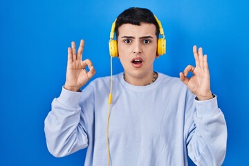 Poster - Non binary person listening to music using headphones looking surprised and shocked doing ok approval symbol with fingers. crazy expression