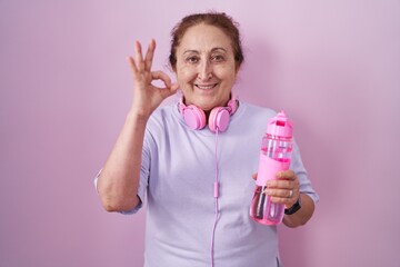 Poster - Senior woman wearing sportswear and headphones smiling positive doing ok sign with hand and fingers. successful expression.