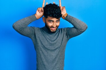 Poster - Arab man with beard wearing turtleneck sweater posing funny and crazy with fingers on head as bunny ears, smiling cheerful