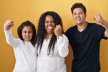 Sticker - Family of mother, daughter and son standing over yellow background angry and mad raising fist frustrated and furious while shouting with anger. rage and aggressive concept.