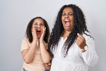 Sticker - Mother and young daughter standing over white background shouting angry out loud with hands over mouth