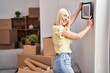 © Krakenimages.com - Young blonde woman smiling confident hanging frame on wall at new home