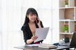 © amnaj - Charming and smiling Asian businesswoman chatting on mobile phone with customer in office.