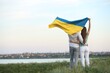 © New Africa - Friends holding national flag of Ukraine in field, back view. Space for text