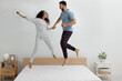 © New Africa - Happy couple jumping on bed with comfortable mattress at home