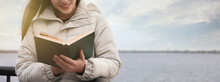 Woman Reading Book Near River On Cloudy Day, Space For Text. Banner Design