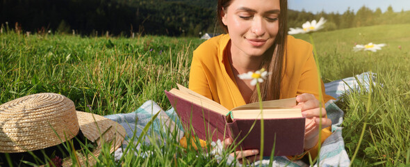 Canvas Print - Beautiful young woman reading book on green meadow in mountains. Banner design