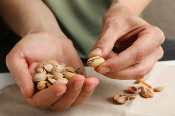 Woman holding tasty roasted pistachio nuts at table, closeup