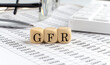 wooden cubes with the word GFR - Glomerular Filtration Rate on a financial background with chart, calculator, pen and glasses, business concept.