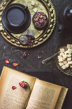 Still Life With Cup Of Tea Place With Dry Flowers, Sugar Black Tea Pot And Vintage Book On Rustic Dark Background