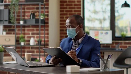 Poster - Company employee writing online report on documents to create business project. Office worker with face mask taking notes on paperwork to plan statistics data on laptop app, browsing internet.