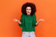 What Do You Want? Woman With Afro Hairstyle Wearing Green Casual Sweater Asking Who Why Make This Conflict, Looking With Annoyed Indignant Expression. Indoor Studio Shot Isolated On Orange Background.