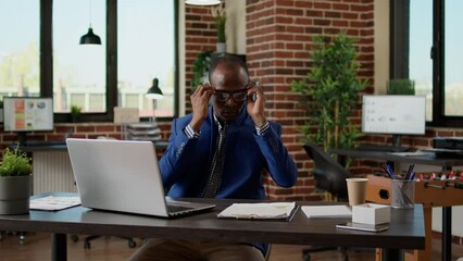 Poster - African american employee taking notes on documents and laptop, working on startup project. Executive manager writing data report on computer, typing email on website browser app.