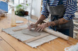 © DimaBerlin - Craft artist making object out of clay in studio, cropped shot. Female ceramic artist with tattoo on hands use fettling knife to cut and trim clay, creating handmade kitchenware at pottery workshop