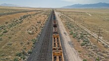 Flying Over Train Tracks With Empty Cars In The Utah Desert Disappearing Into The Horizon.