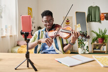 Teen Blogger Recording Video And Playing Violin For His Blog On Smartphone On Tripod At Home