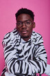 Portrait of African teenage boy in stylish hoodie with zebra print looking at camera against pink background