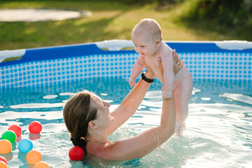 Family playing with balls toys in the swimming pool. Kids having fun in the pool. Summer leisure and holidays and vacation concept. People swim in a metal frame pool on a green grass lawn.