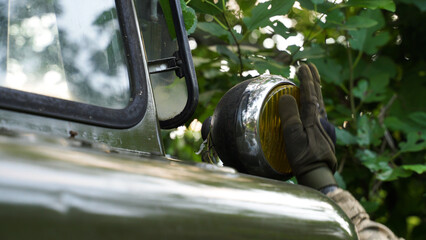 a soldier in a camouflage uniform and tactical gloves wipes the headlight of a military truck. preparation of military vehicles for a combat mission. special equipment lighting.