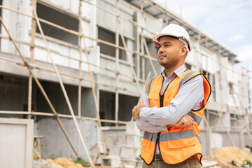 Confident engineer handsome man standing arms crossed at modern home building construction. Architect with white safety helmet at construction site.