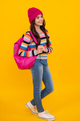 Winter school holiday. Back to school. Teenager schoolgirl with warm hat and sweater on yellow isolated studio background. Winter school. Happy teenager, positive and smiling school girl.