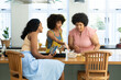 © wavebreak3 - Biracial woman with smartphone looking at friends with afro hair making pizza at kitchen island